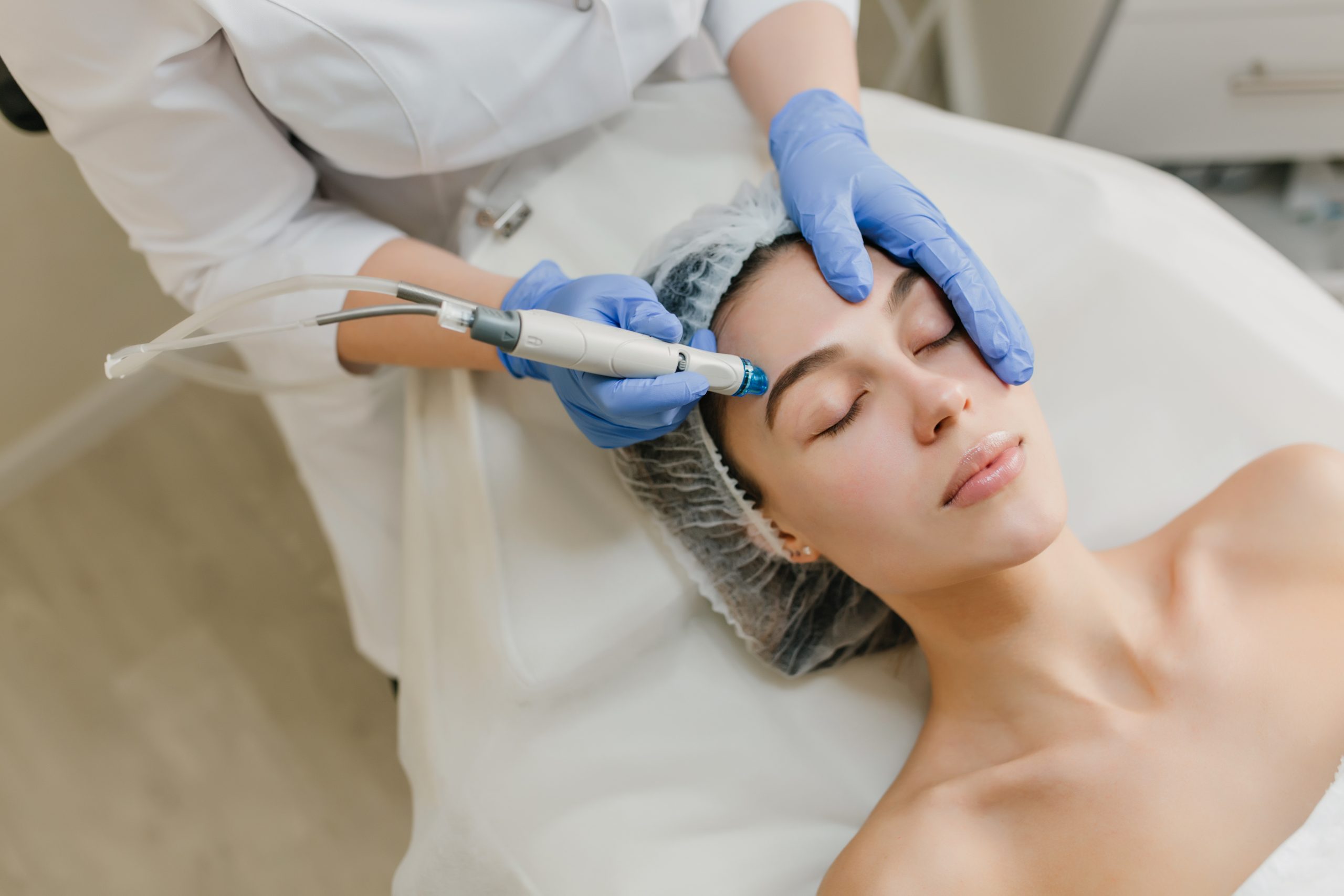 View from above rejuvenation of beautiful woman enjoying cosmetology procedures in beauty salon. Dermatology, hands in blue glows, healthcare, therapy, botox. https://queenbeauty.fi/wp-content/uploads/2024/02/аквапил-2-scaled.jpg